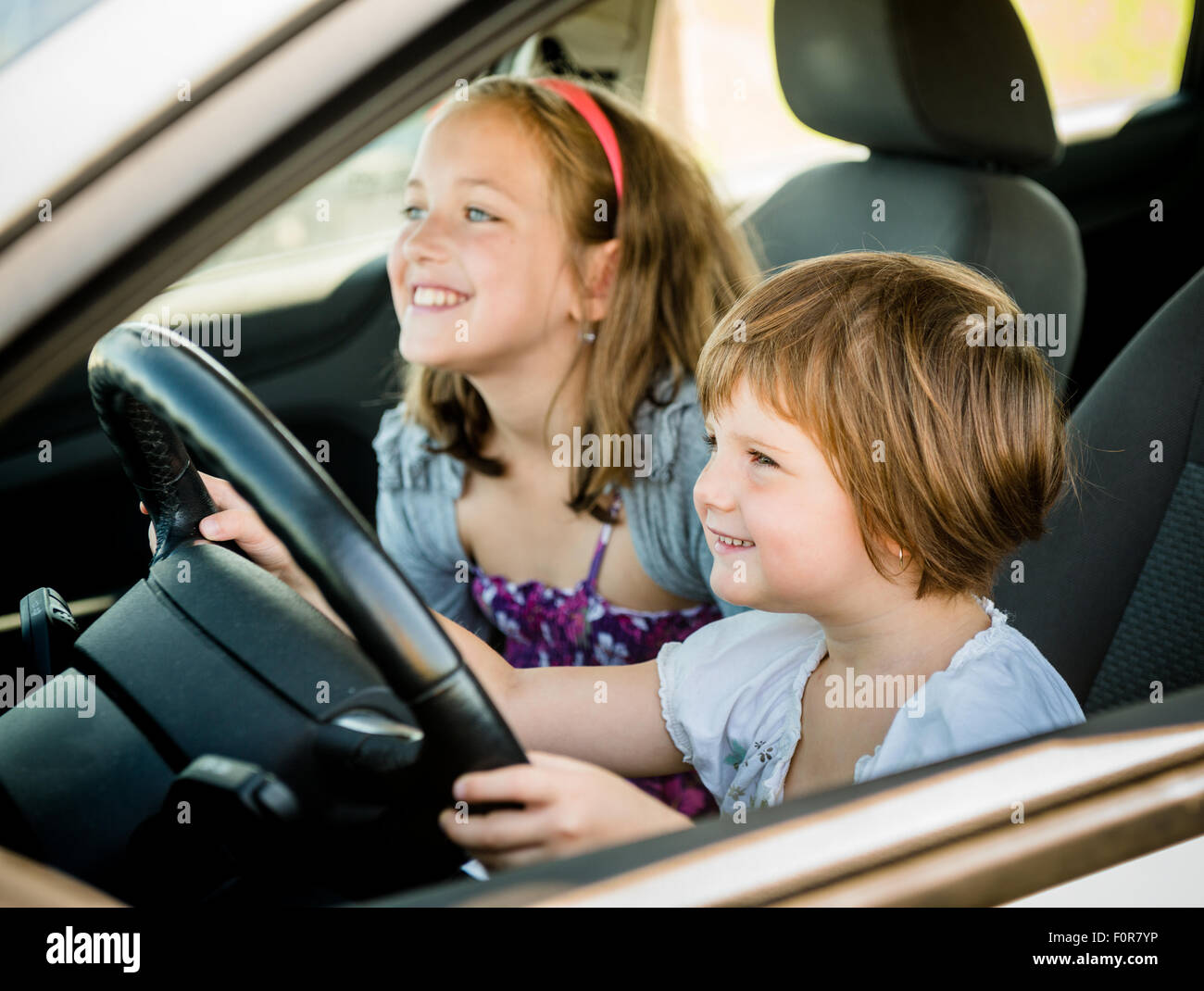 Children pretend driving car sitting on front vehicle seats Stock Photo