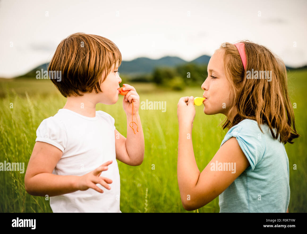 Children blowing on each other in whistles - outdoor in nature Stock Photo