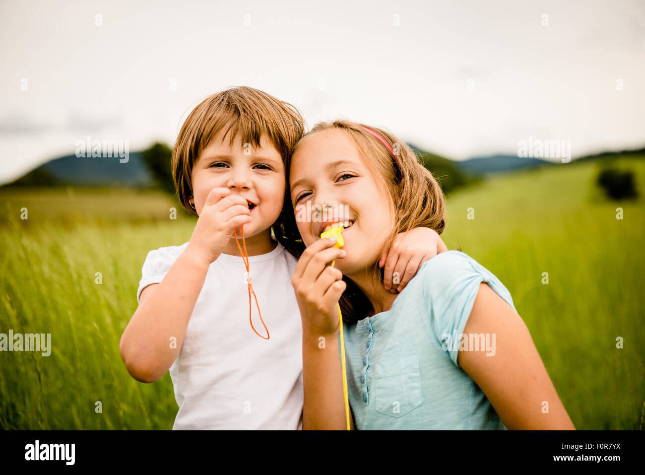 Children blowing together in whistles - outdoor in nature Stock Photo