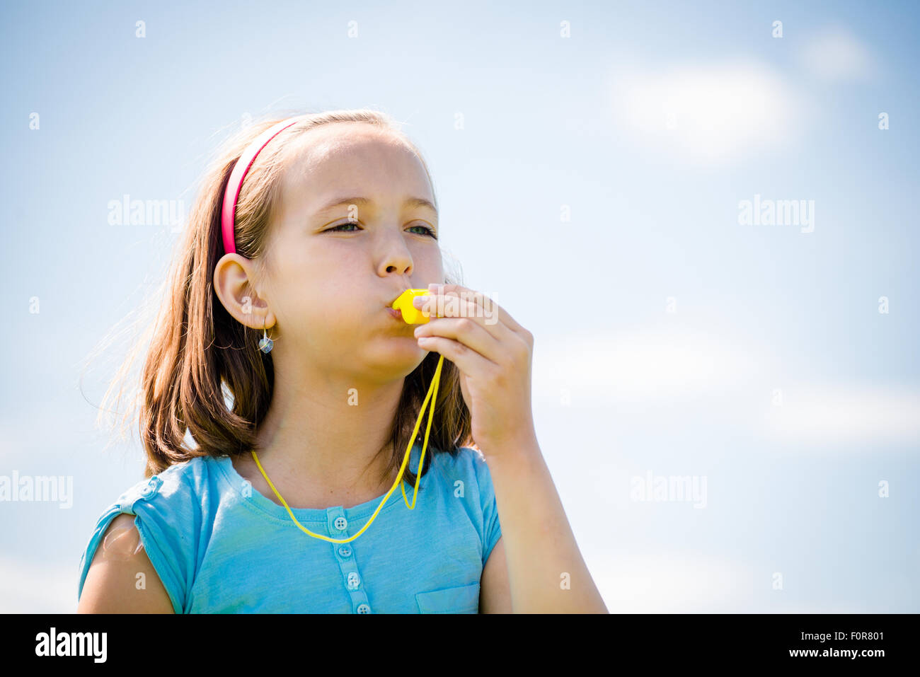 Beautiful child blowing in whistle - outdoor with blue sky Stock Photo