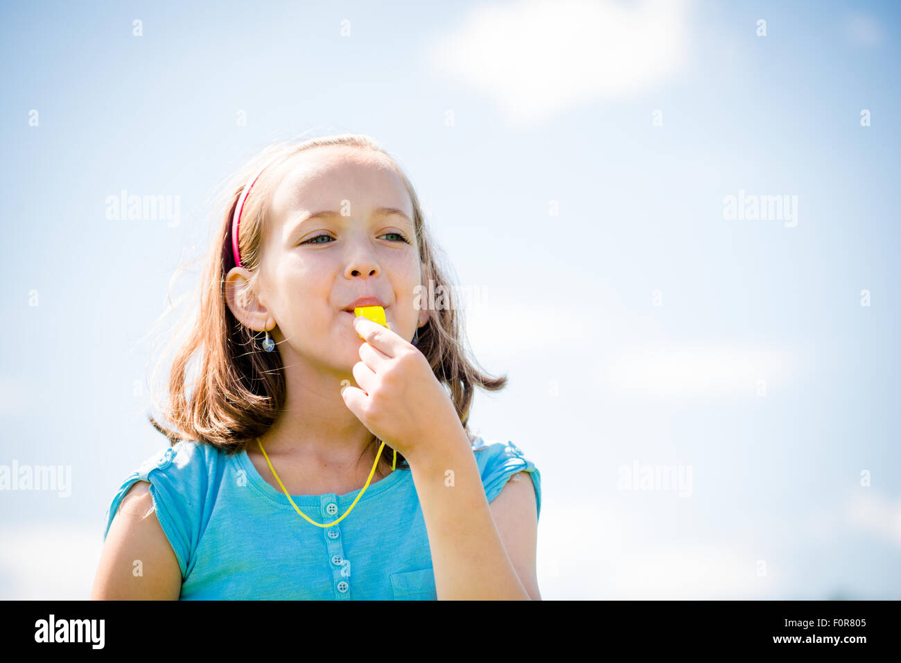 Cute teen girl blowing in whistle - blue sky in background Stock Photo
