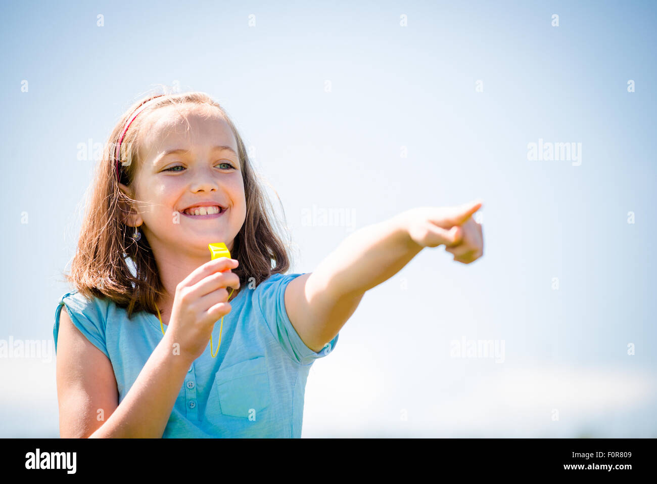 Smiling child blowing in whistle and pointing with hand - outdoor in nature Stock Photo