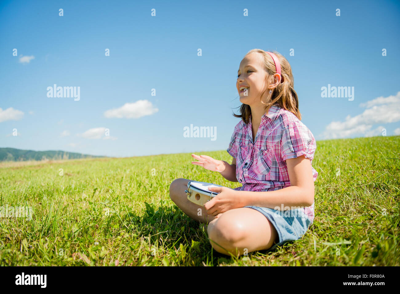 Cute teen girl playing tambourine and singing - outdoor in nature Stock Photo