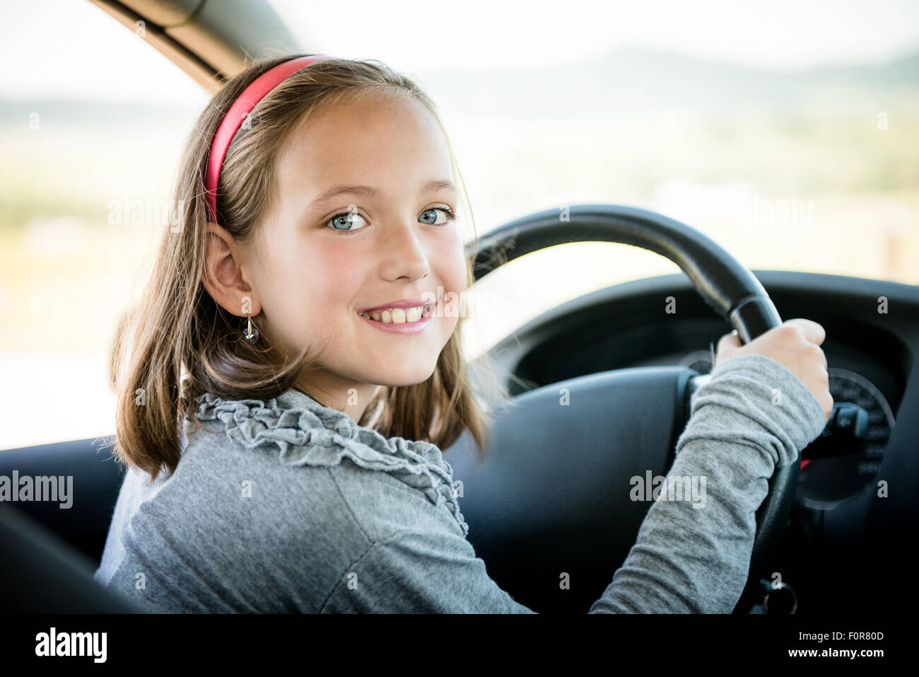 Child pretends driving car sitting on front driver seat with hands on steering Stock Photo