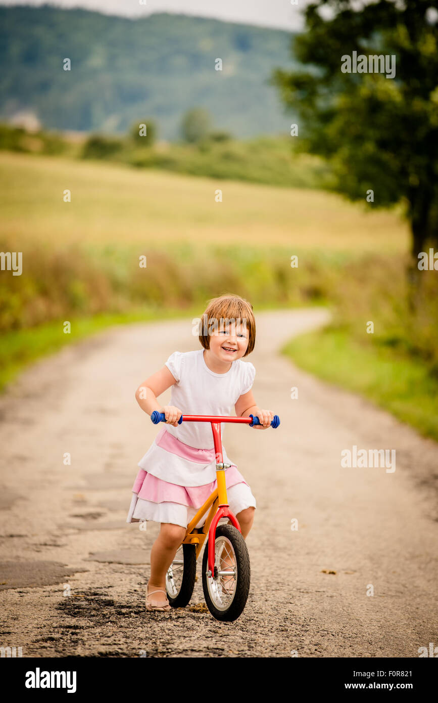 Little child driving her firs bicycle on rural road outdor in nature Stock Photo