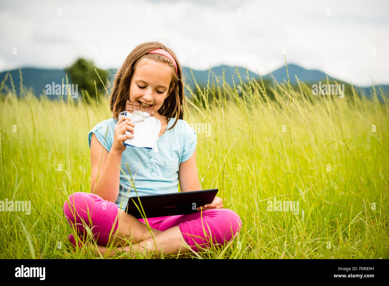Child eating and relishing chocolate while watching tablet - outdoor in nature Stock Photo