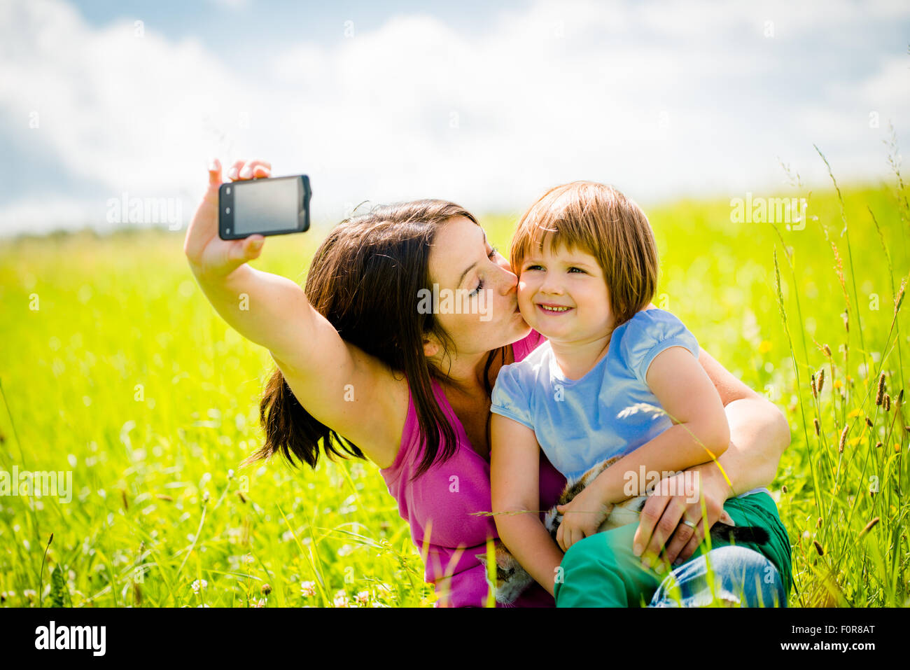 Young woman taking photo with her smart-phone camera of herself, her daughter and kitten Stock Photo