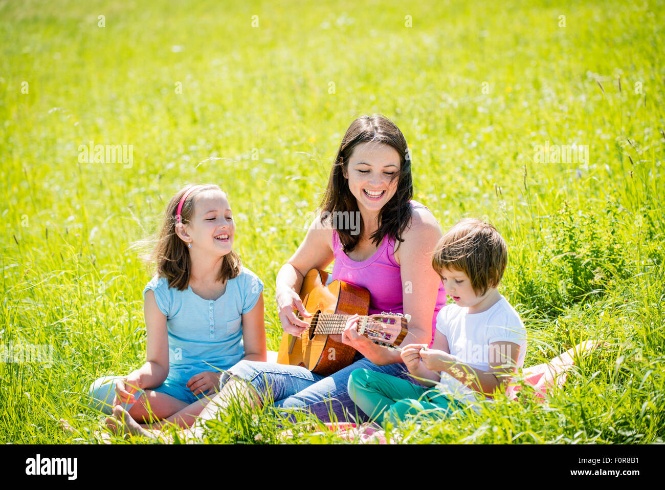 Woman playing guitar to her children in nature on sunny summer day Stock Photo