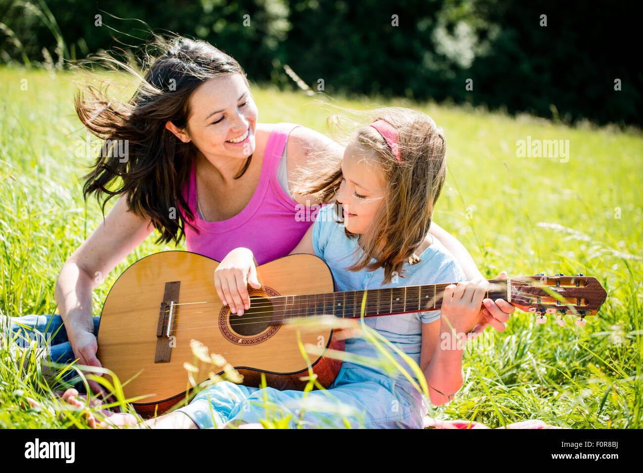 Mother teaches plaing guitar her child - outdoor in nature on sunny day Stock Photo