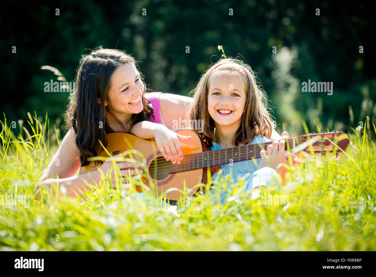 Mother teaches plaing guitar her child - outdoor in nature on sunny day Stock Photo