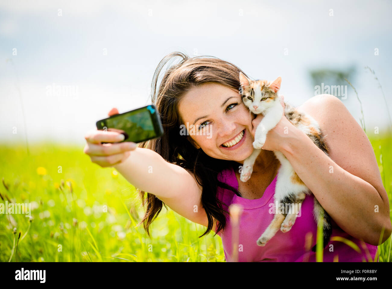 Woman taking photo with mobile phone camera of herself and her cat - outdoor in nature Stock Photo