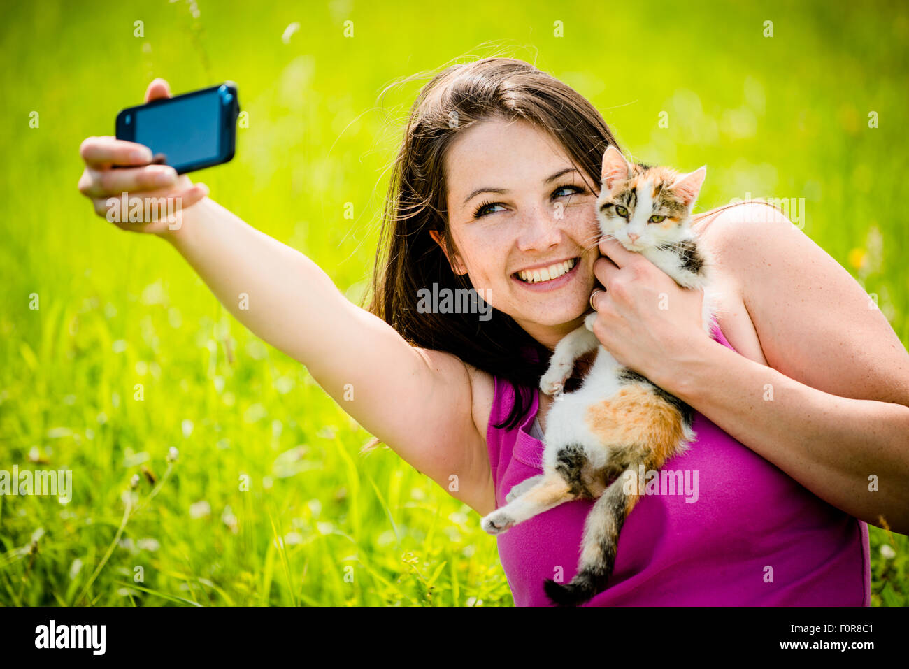 Woman taking photo with mobile phone camera of herself and her cat - outdoor in nature Stock Photo