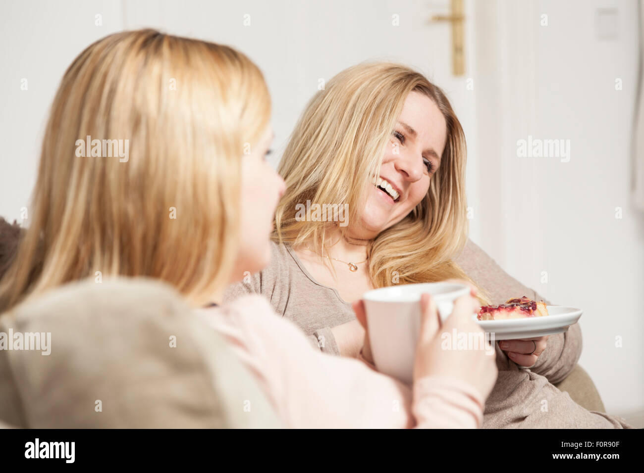 girlfriends talking on sofa and eating cake Stock Photo