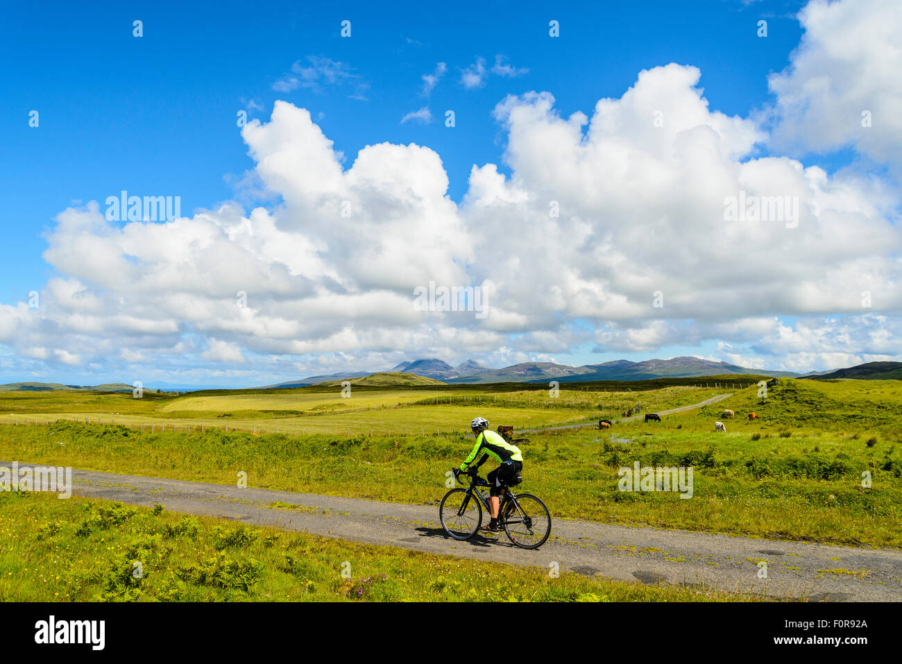 Female cyclist on empty road on the island of Islay Scotland looking to the Paps of Jura Stock Photo