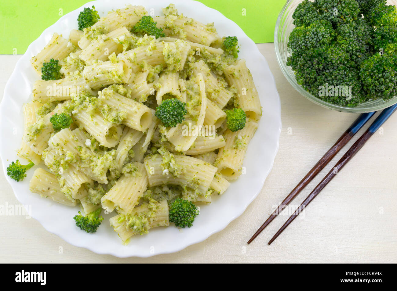 Cooked pasta with broccoli served with cooked broccoli in a white bow on a wooden table. Eating with chopsticks Stock Photo