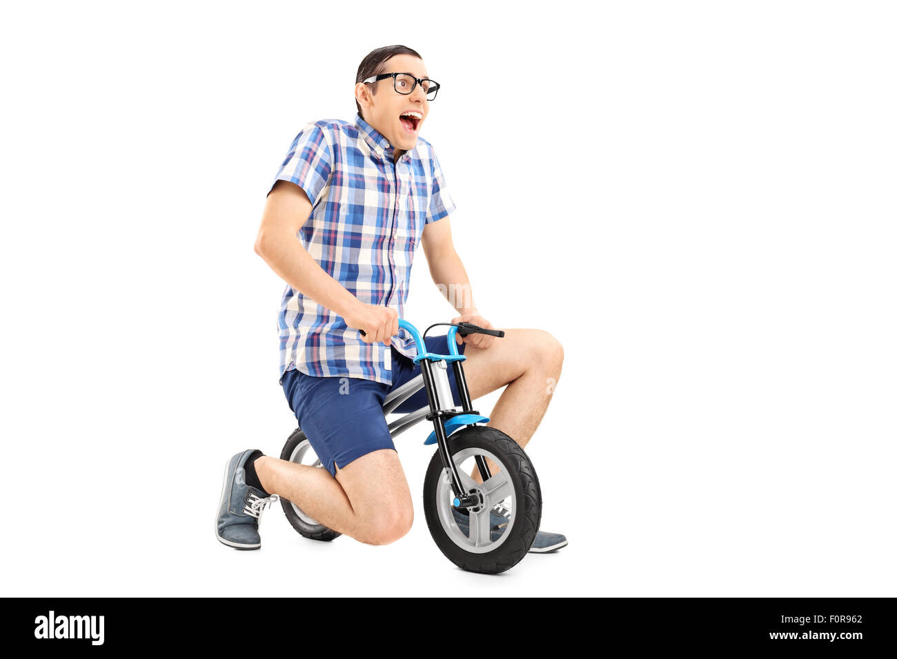 Studio shot of a silly young guy riding a tiny bicycle isolated on white background Stock Photo