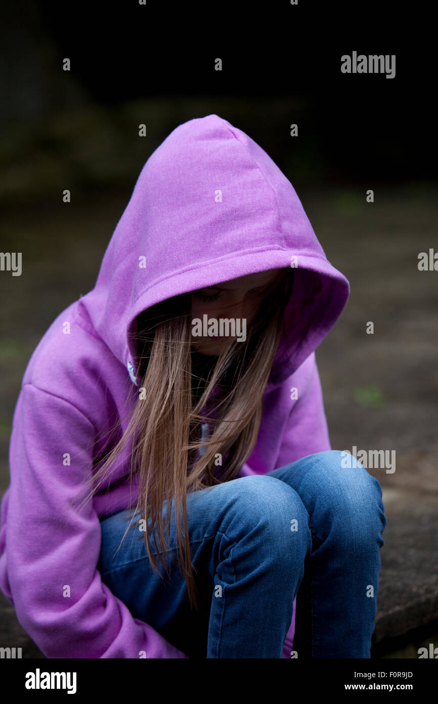 Sad girl in hooded top, sitting with head low in despair Stock Photo