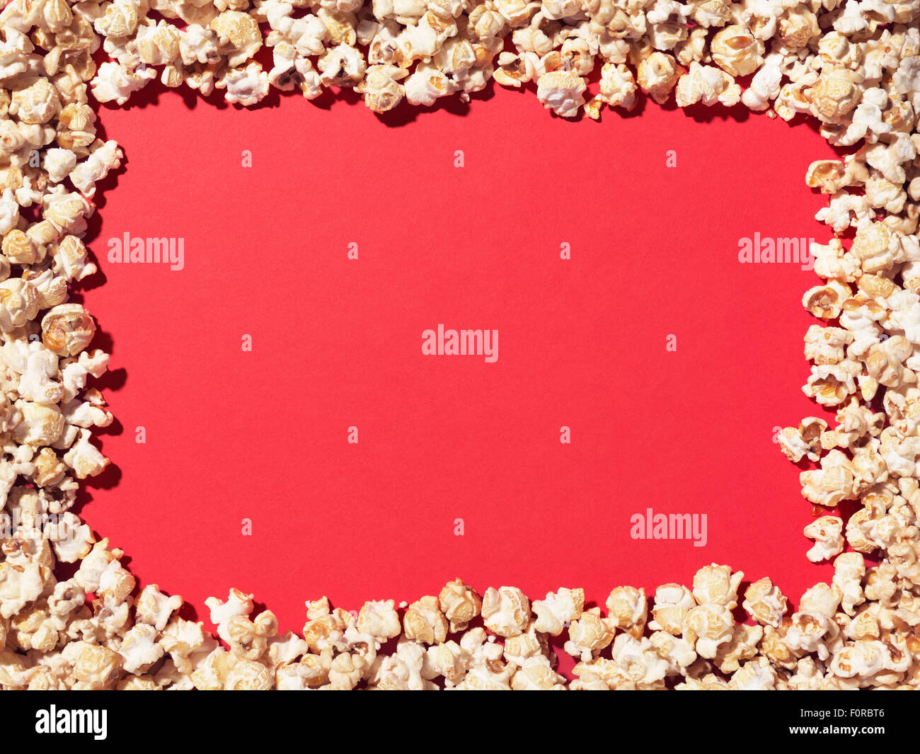 Shot of popcorn arranged to give a border to a plain, red area ideal for designer to add copy. Stock Photo