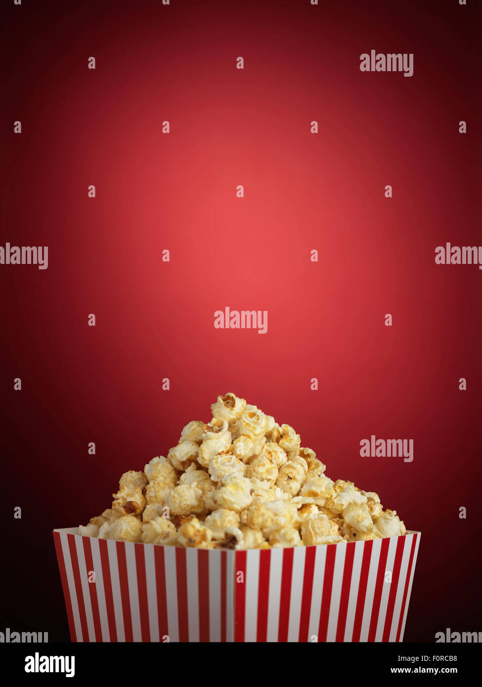 Shot of cinema style popcorn in a traditional striped box on a red background with a lot of copy space in a vignette or halo Stock Photo