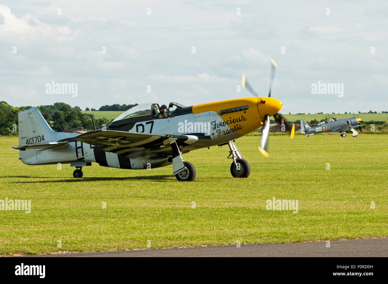 Side view of a Mustang aircraft on an airfield with engine running. Another World War two aircraft is visible in background. Stock Photo