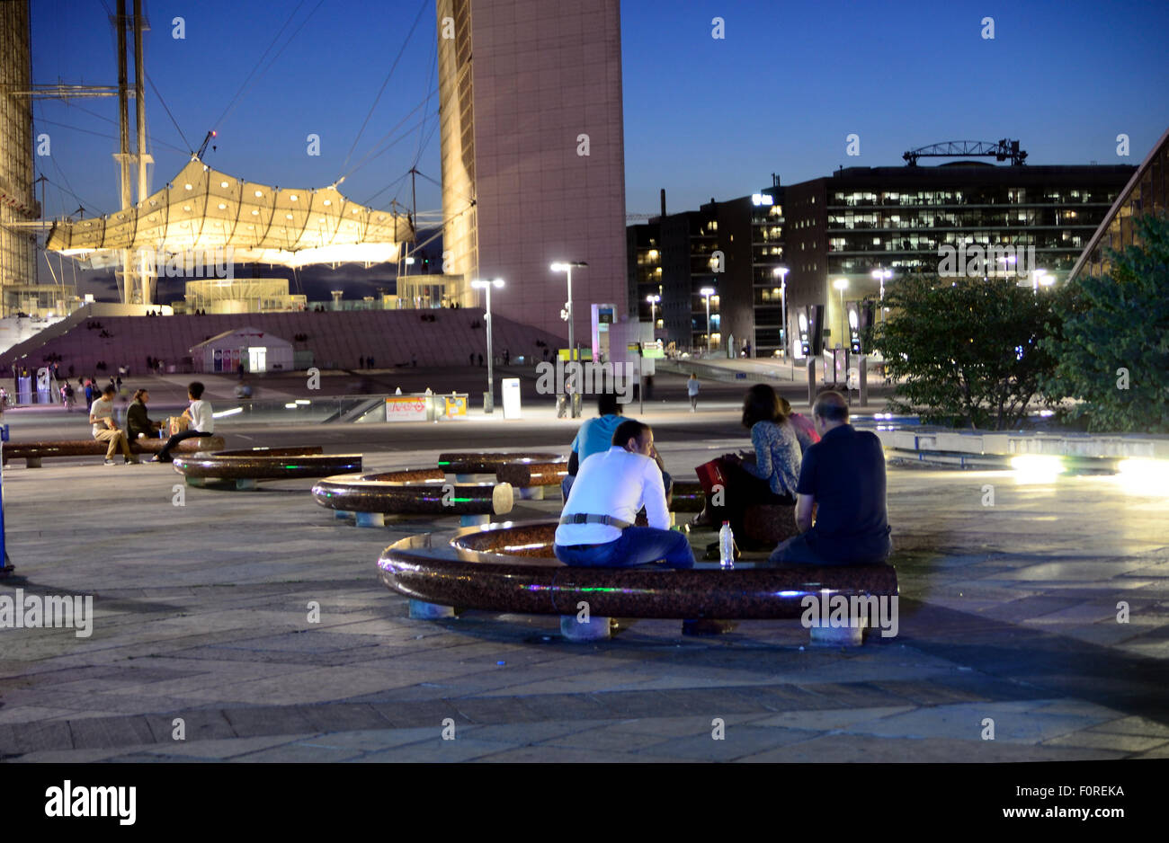 People sit on semicircular benches in the late evening underneath the Grand Arch at La Defense in Paris. Stock Photo