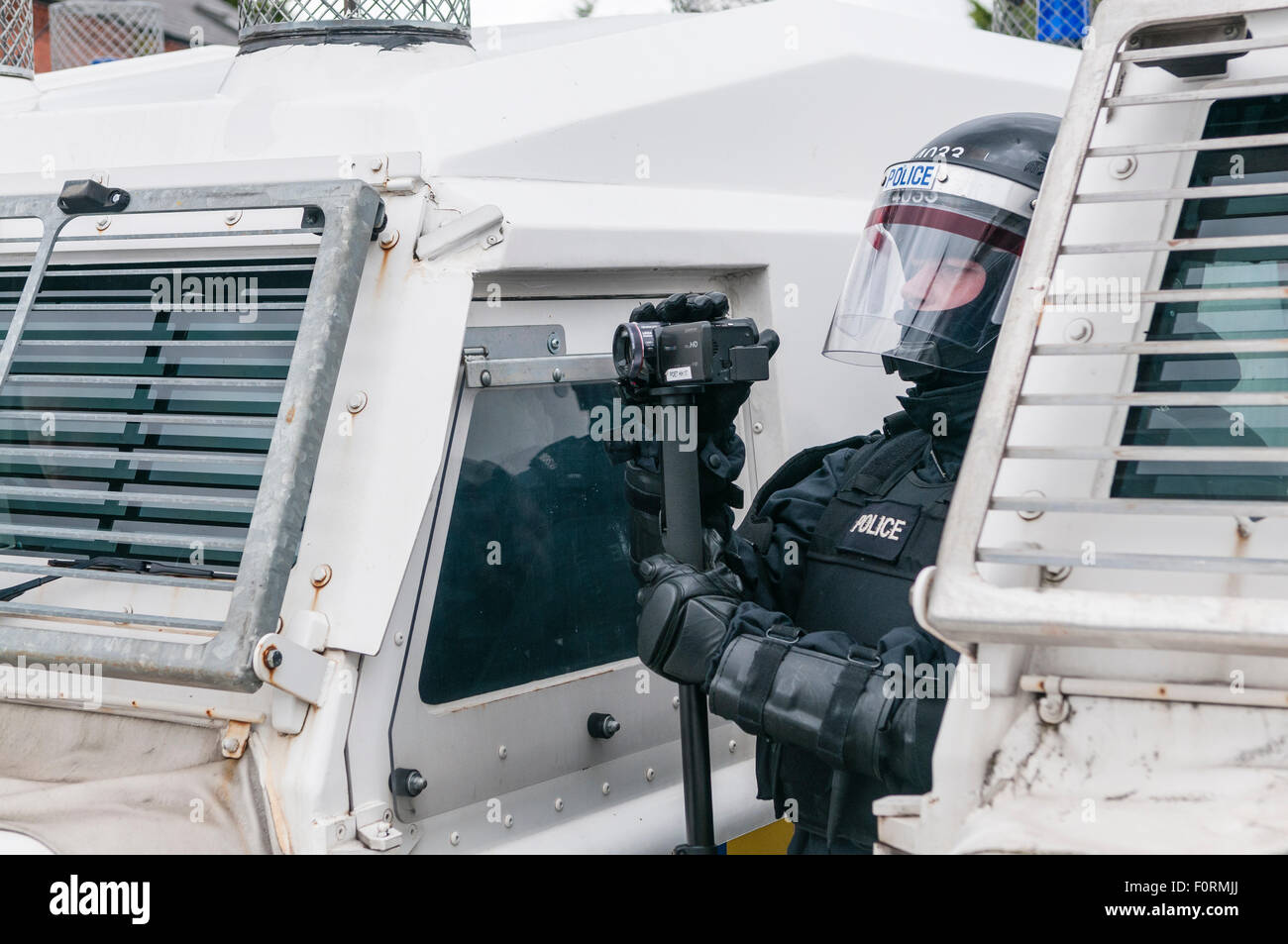 A PSNI police officer dressed in riot uniform uses a video camera to gather evidence during a public disorder riot Stock Photo