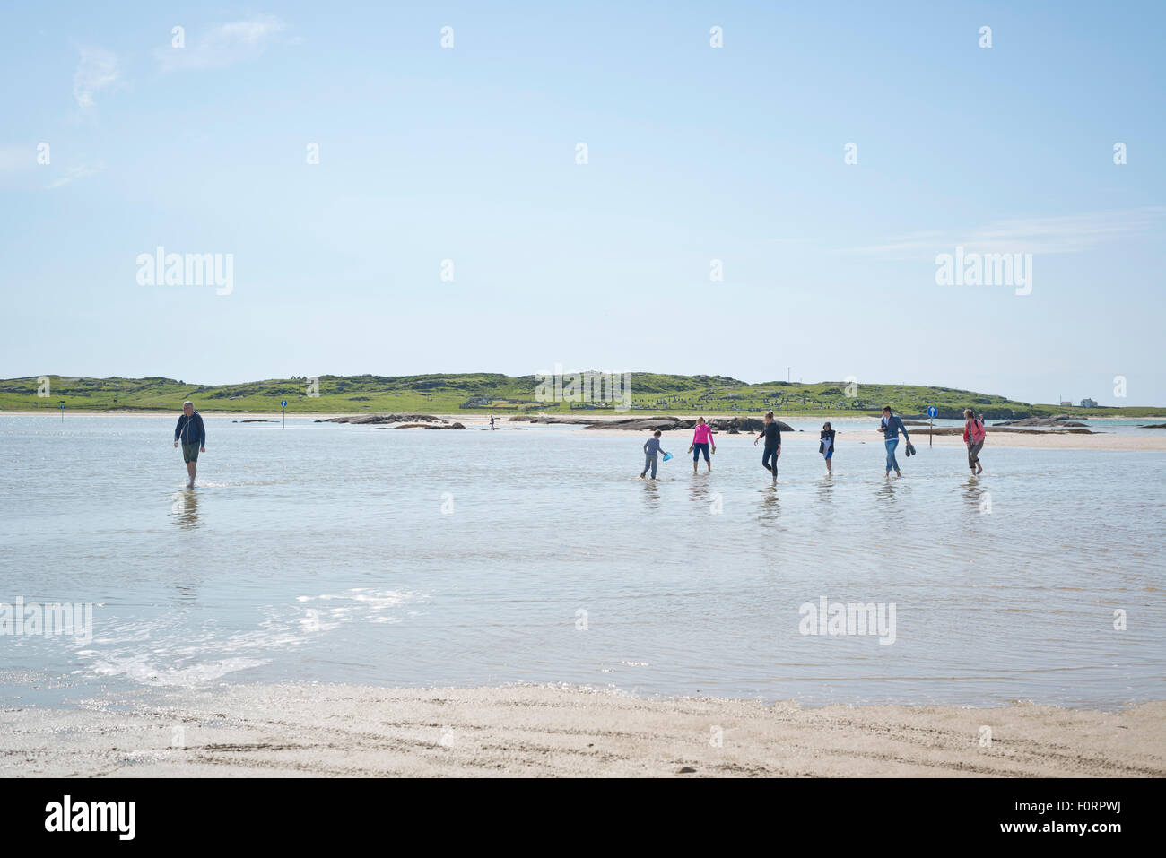 People paddling in the shallow water on the flooded beach route to Omey Island Stock Photo