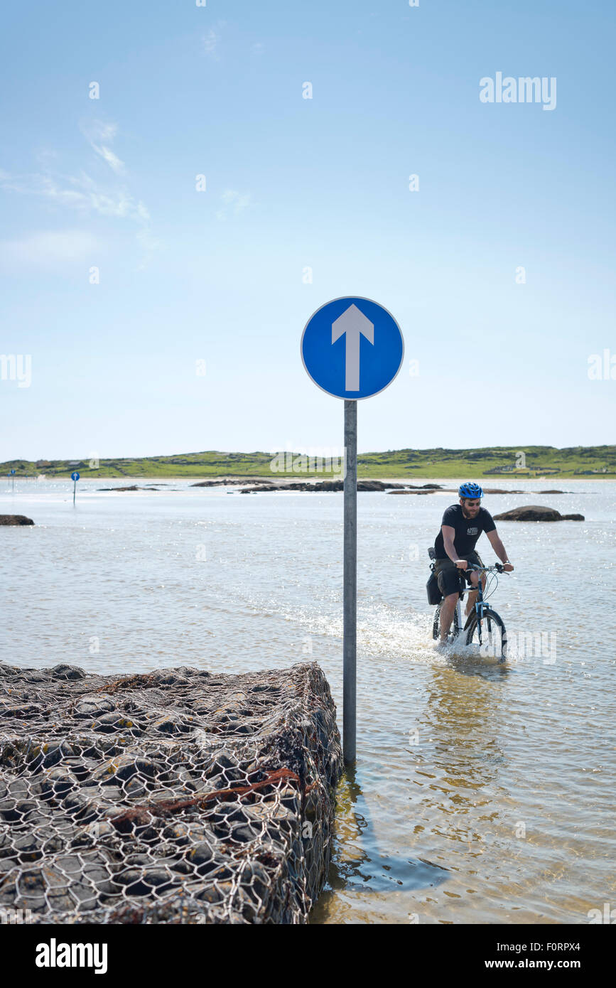 Cyclist on flooded beach route from Omey Island at high tide Stock Photo