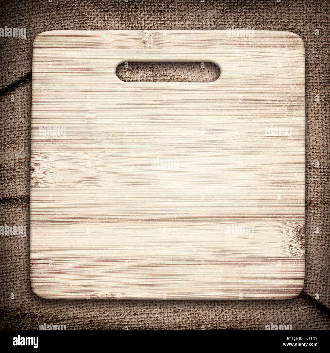 Old cutting board used for cooking on brown crumple burlap tablecloth Stock Photo