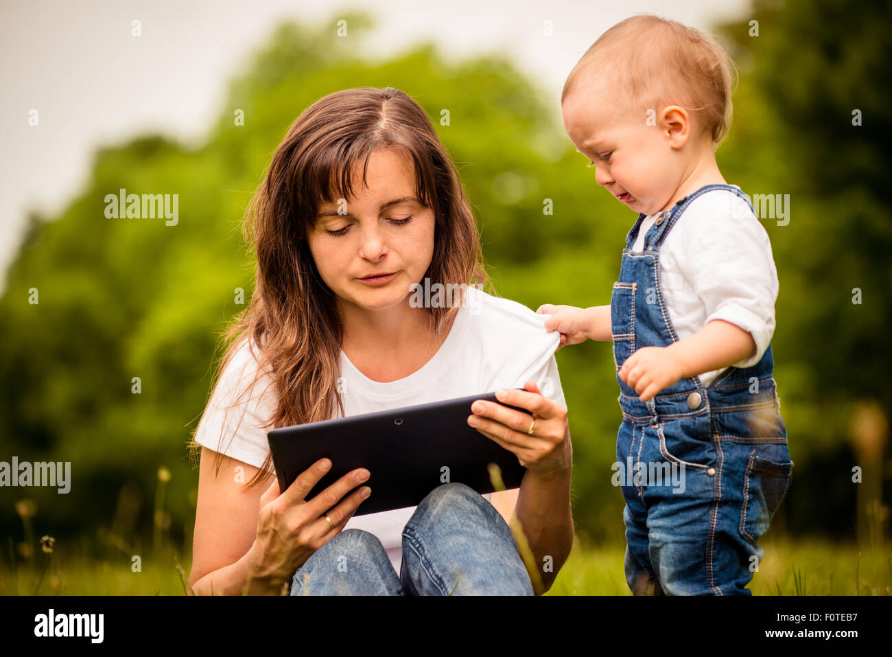 Mother addicted on internet working with tablet while child is trying to draw her attention Stock Photo