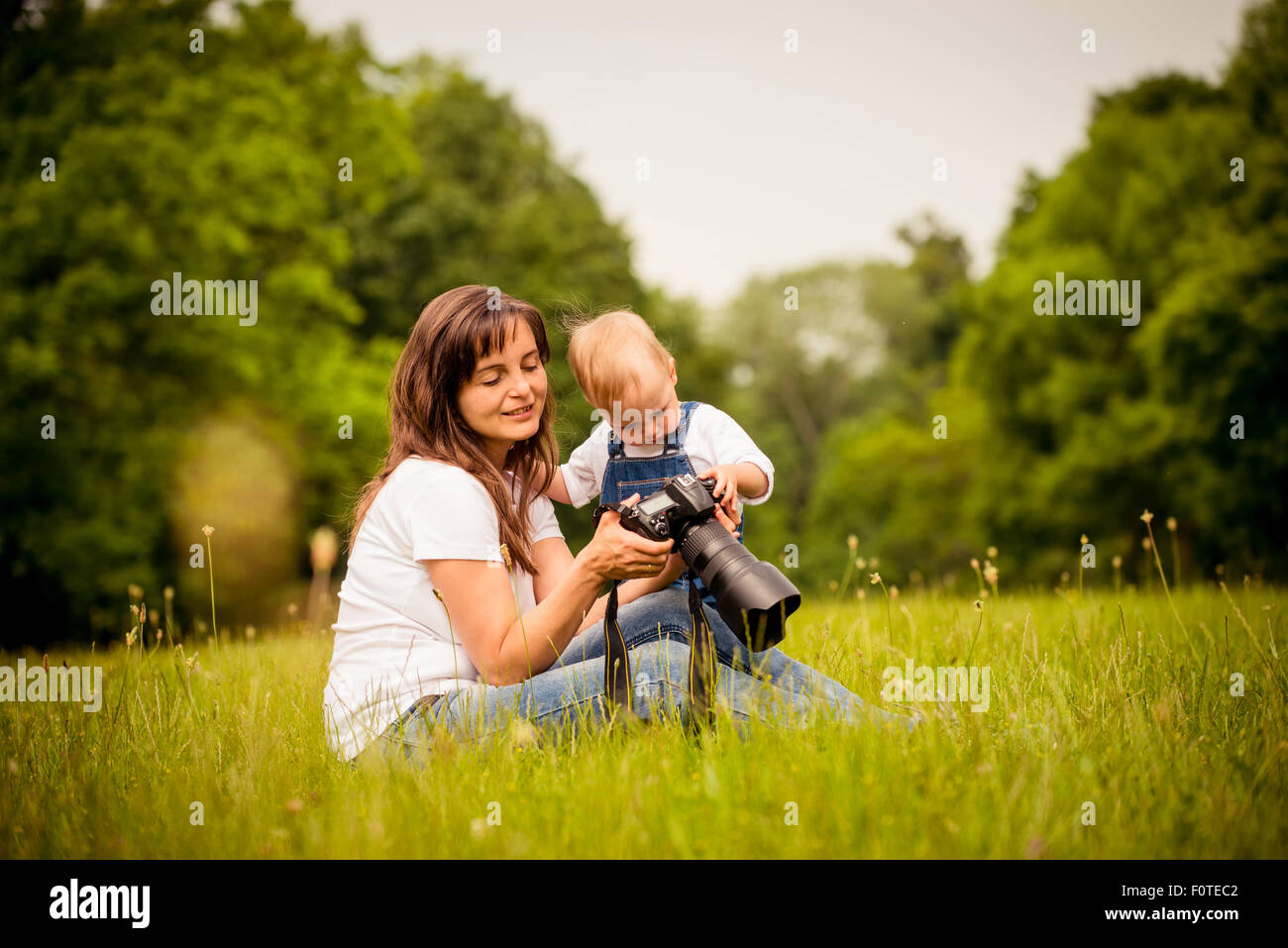 Mother showing her kid captured photos on dslr camera outdoor in nature Stock Photo