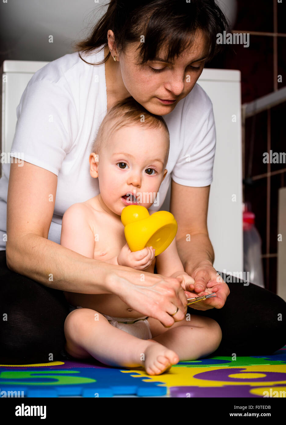Mother cutting fingernails of her child while baby is playing with toys Stock Photo