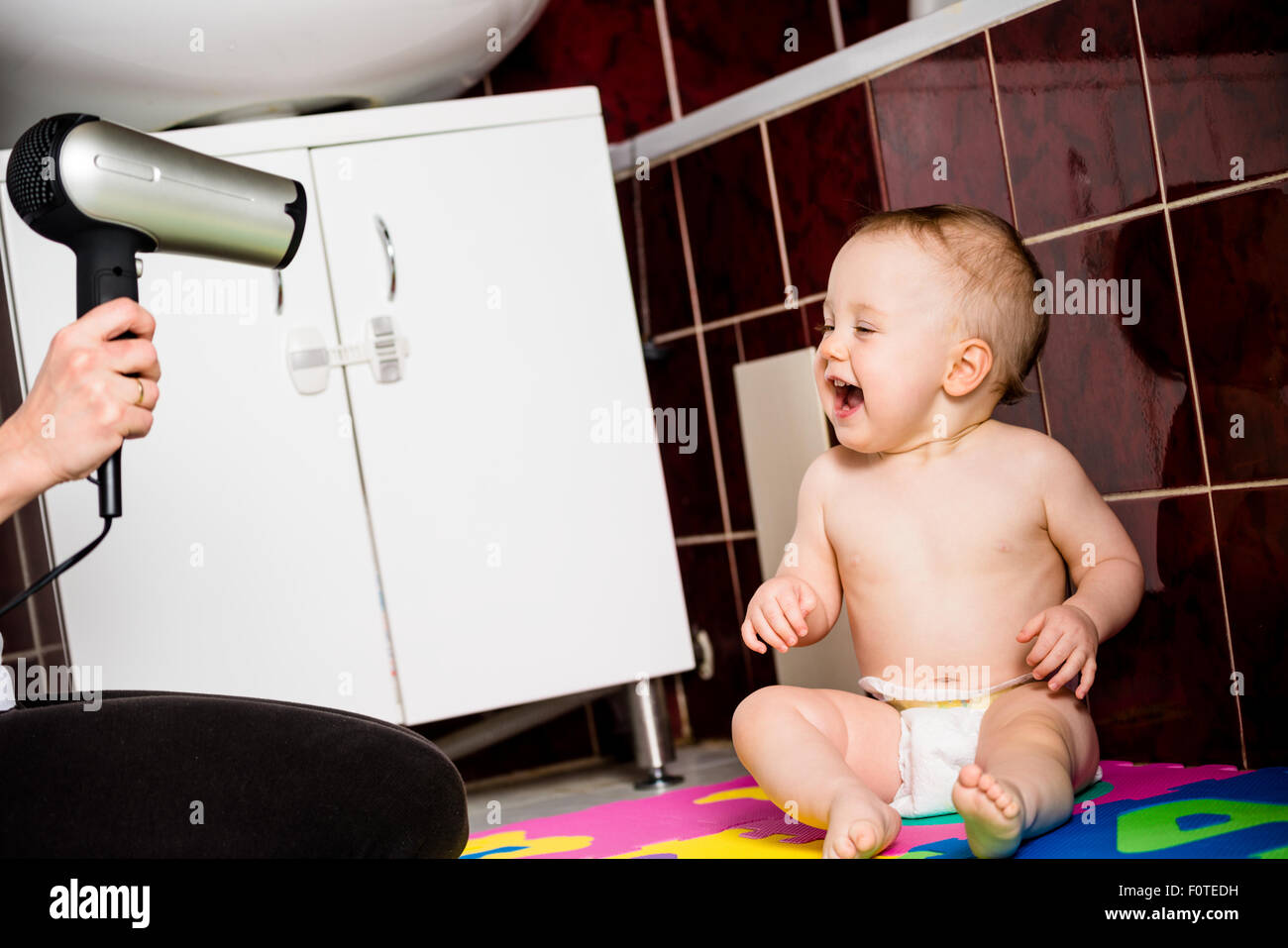 Mother drying hair of her child with hairdryer in bathroom Stock Photo