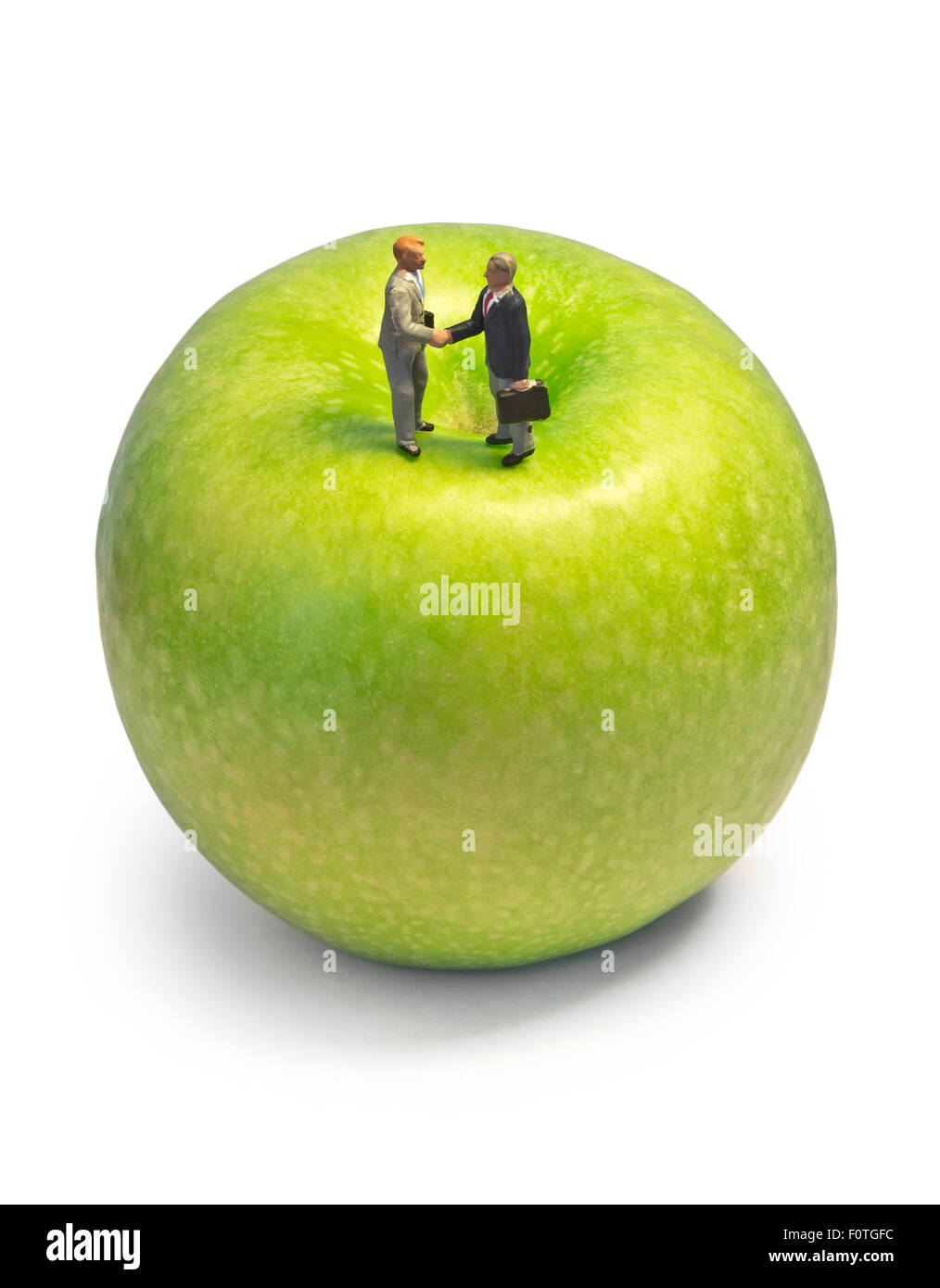 Miniature handshake apple, macro shot of business men figurines shaking hands on top of green apple Stock Photo