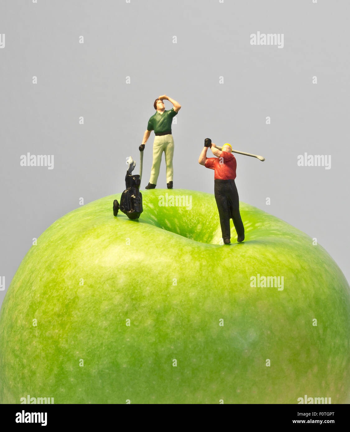 Miniature golf on apple, macro shot of golfing figurines playing round on top of green apple Stock Photo