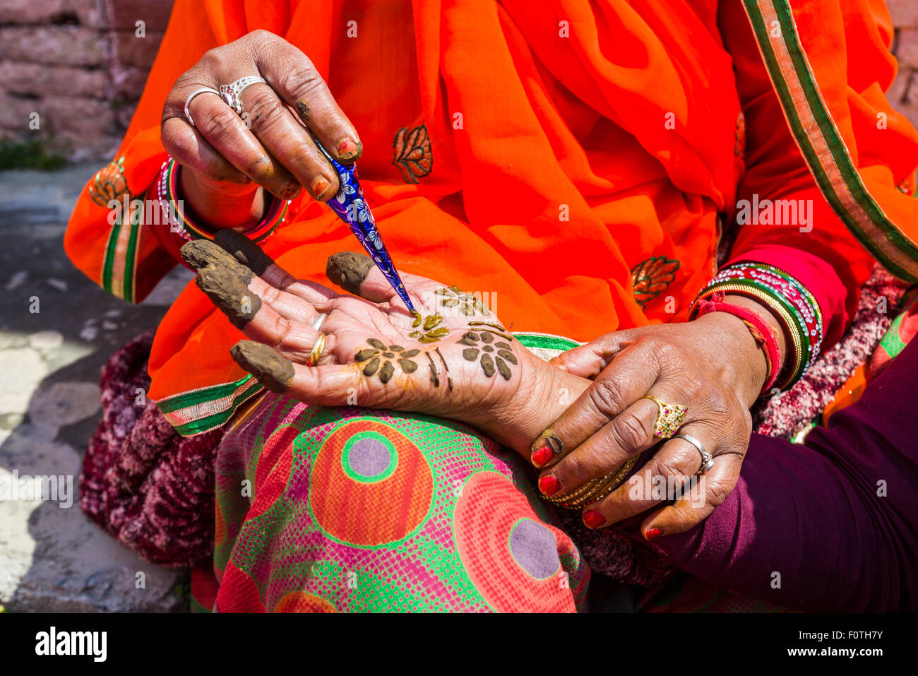 An indian woman is painting a hand with henna, in front of Badrinath Temple, one of the Dschar Dham destinations, Badrinath Stock Photo