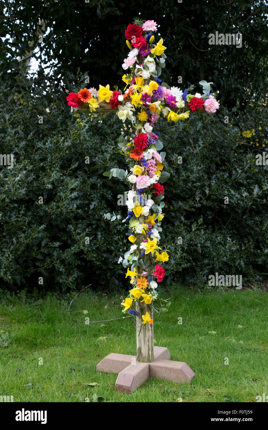 Easter cross covered in colourful flowers outside Cotswold church UK Stock Photo