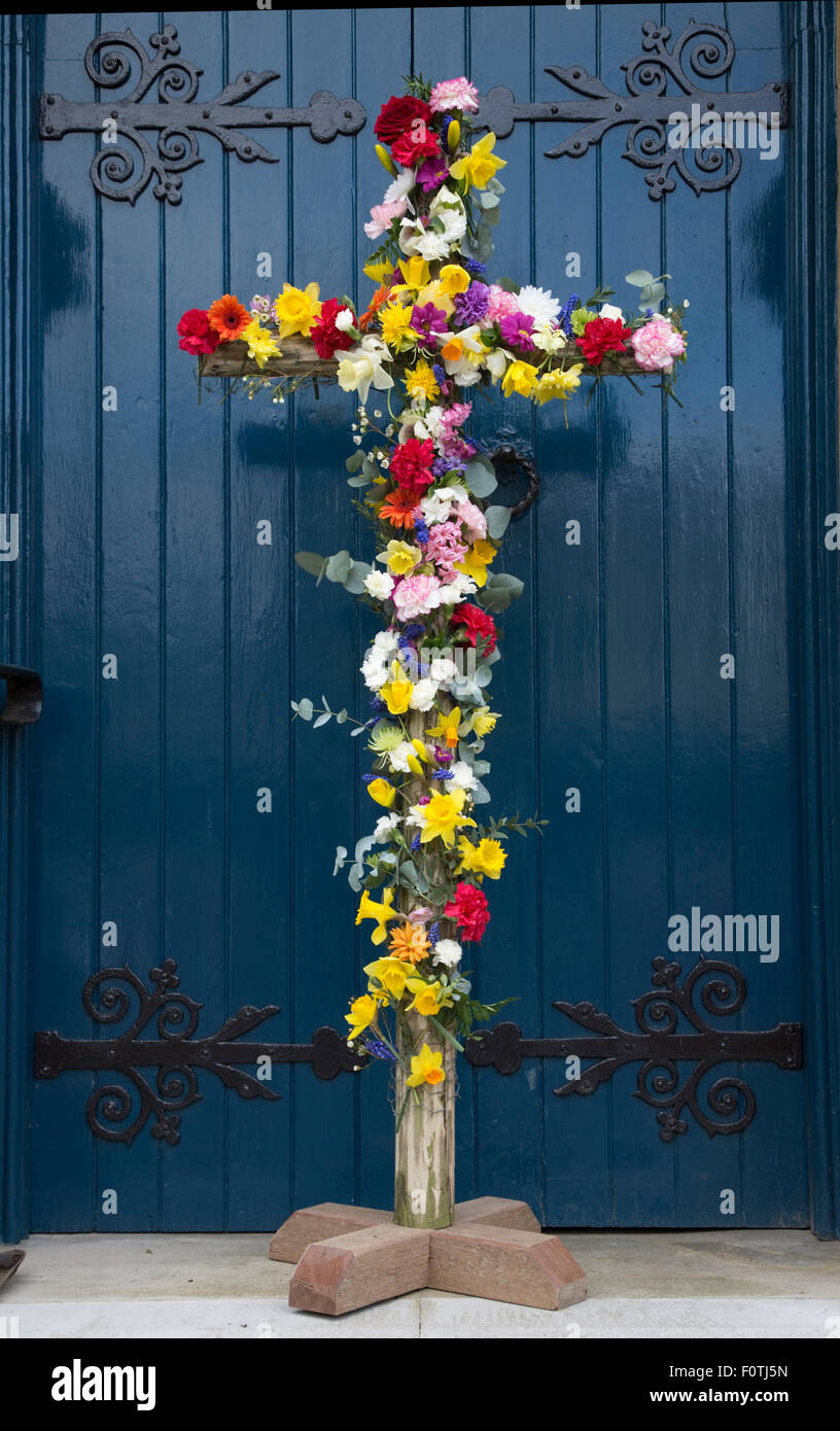 Easter cross covered in colourful flowers outside door of Cotswold church UK Stock Photo
