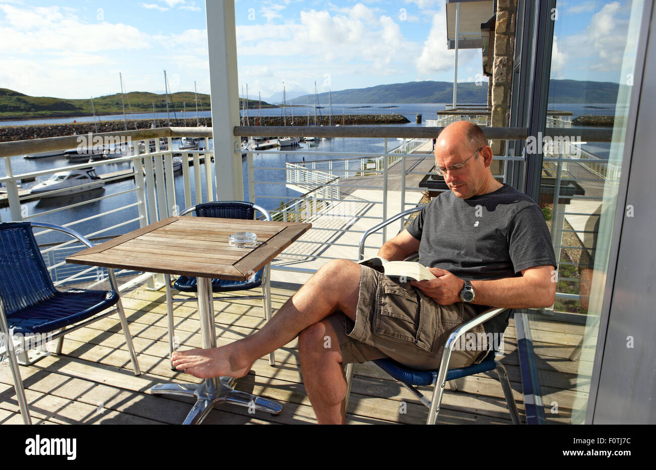 Man relaxing reading a book on a balcony in Portavadie Marina in Scotland on Loch Fyne Stock Photo