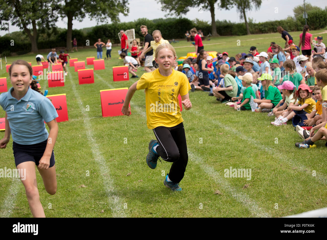 Girls competing in hurdles race with children watching School Sports Day Chipping Campden UK Stock Photo