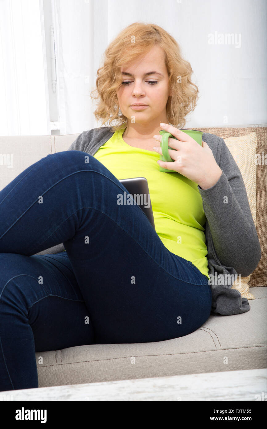A Young Plus Size Woman With A Tablet Pc Sitting On A Sofa Stock