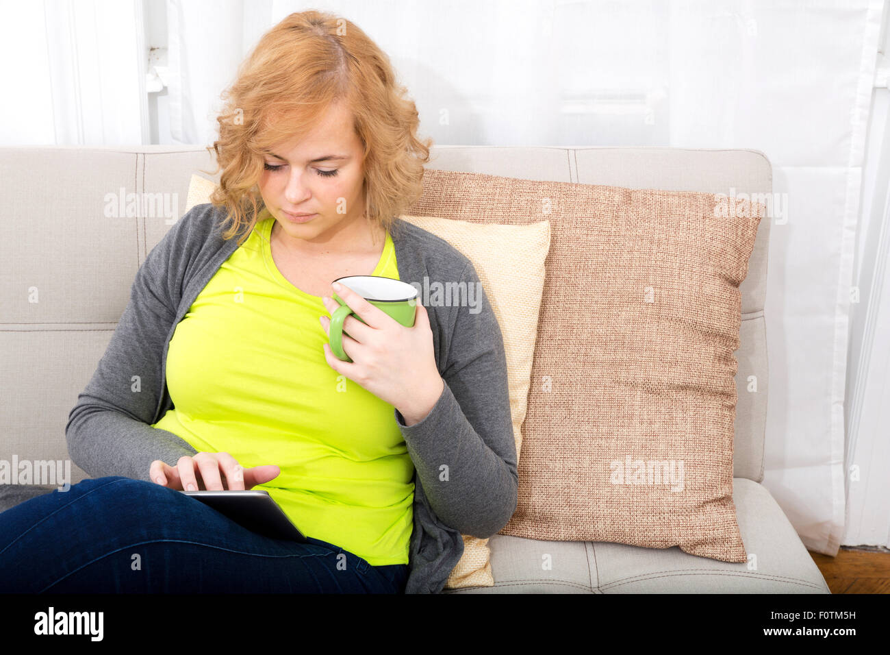 A Young Plus Size Woman With A Tablet Pc Sitting On A Sofa Stock