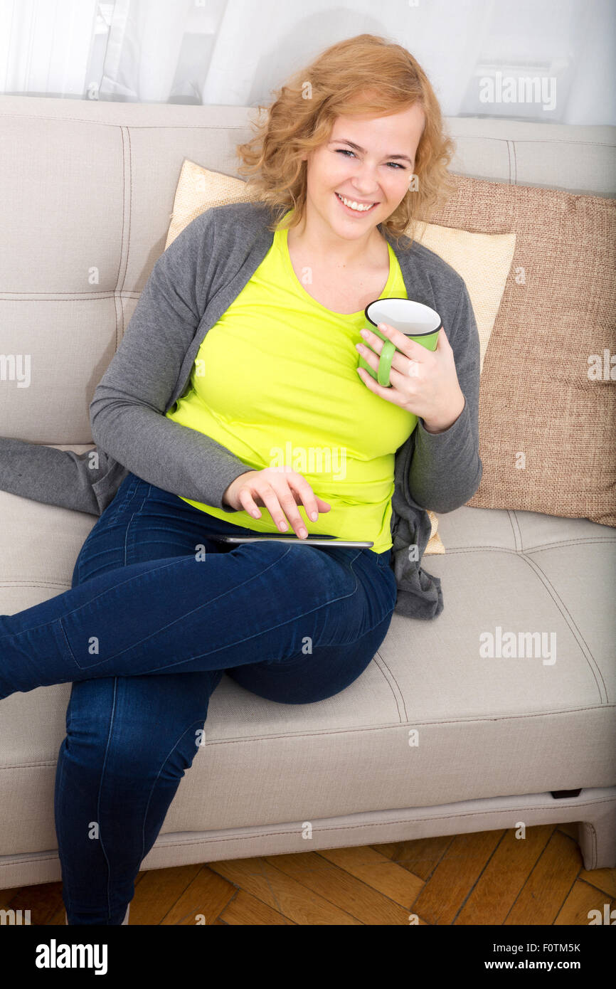 A Young Plus Size Woman With A Tablet Pc Sitting On A Sofa Stock