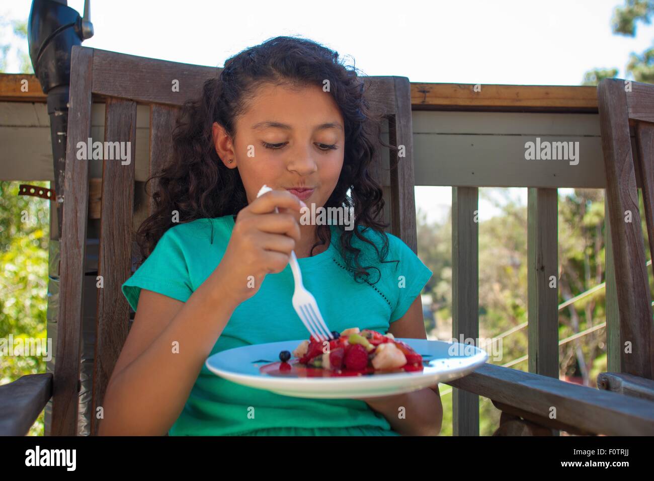 Girl eating fruit dessert on garden bench Stock Photo