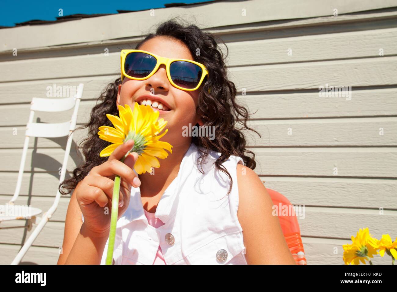 Portrait of girl wearing yellow sunglasses holding sunflower on patio ...