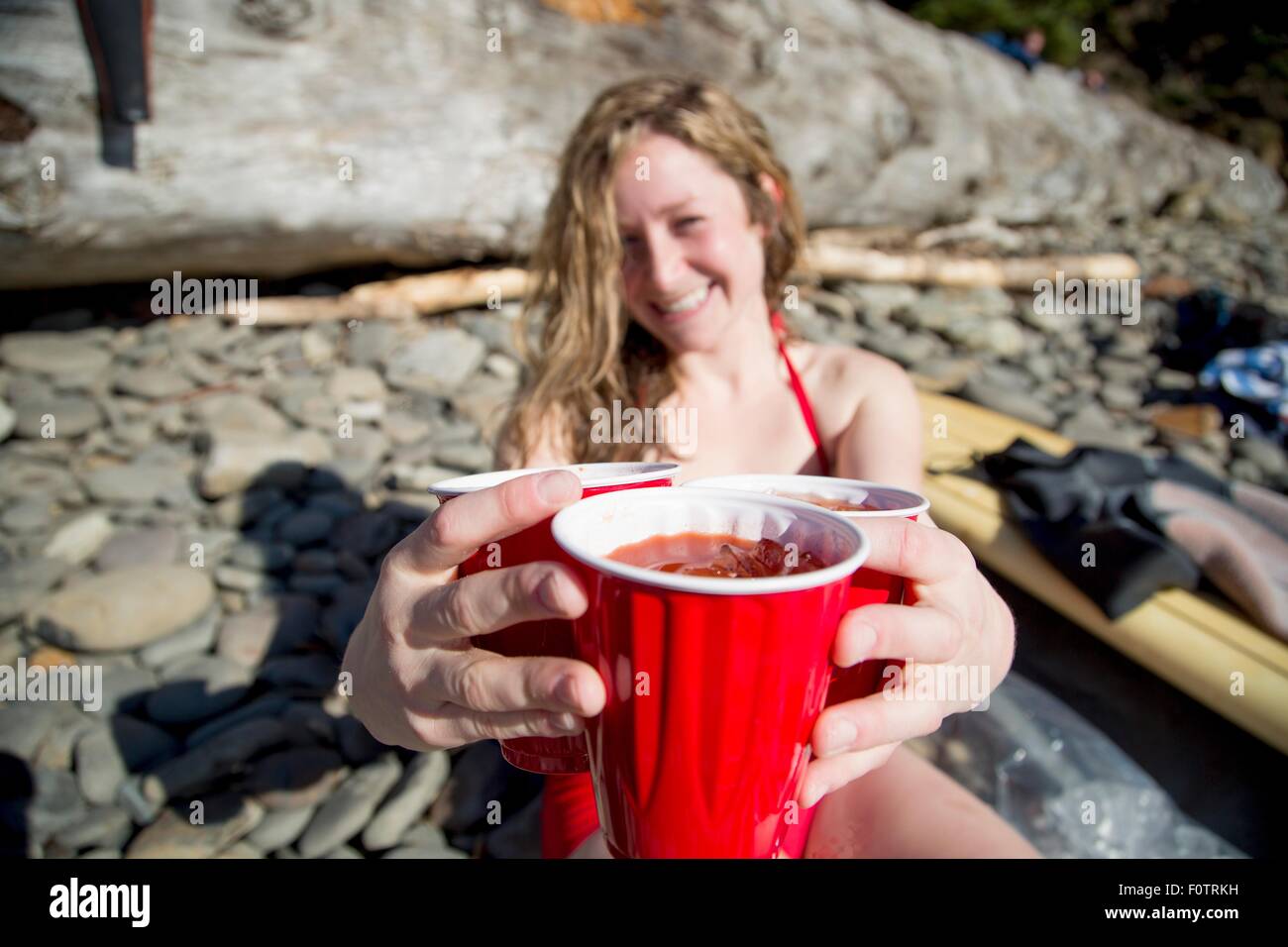 Young woman sitting on rocky beach, holding drinks, smiling, Short Sands Beach, Oregon, USA Stock Photo
