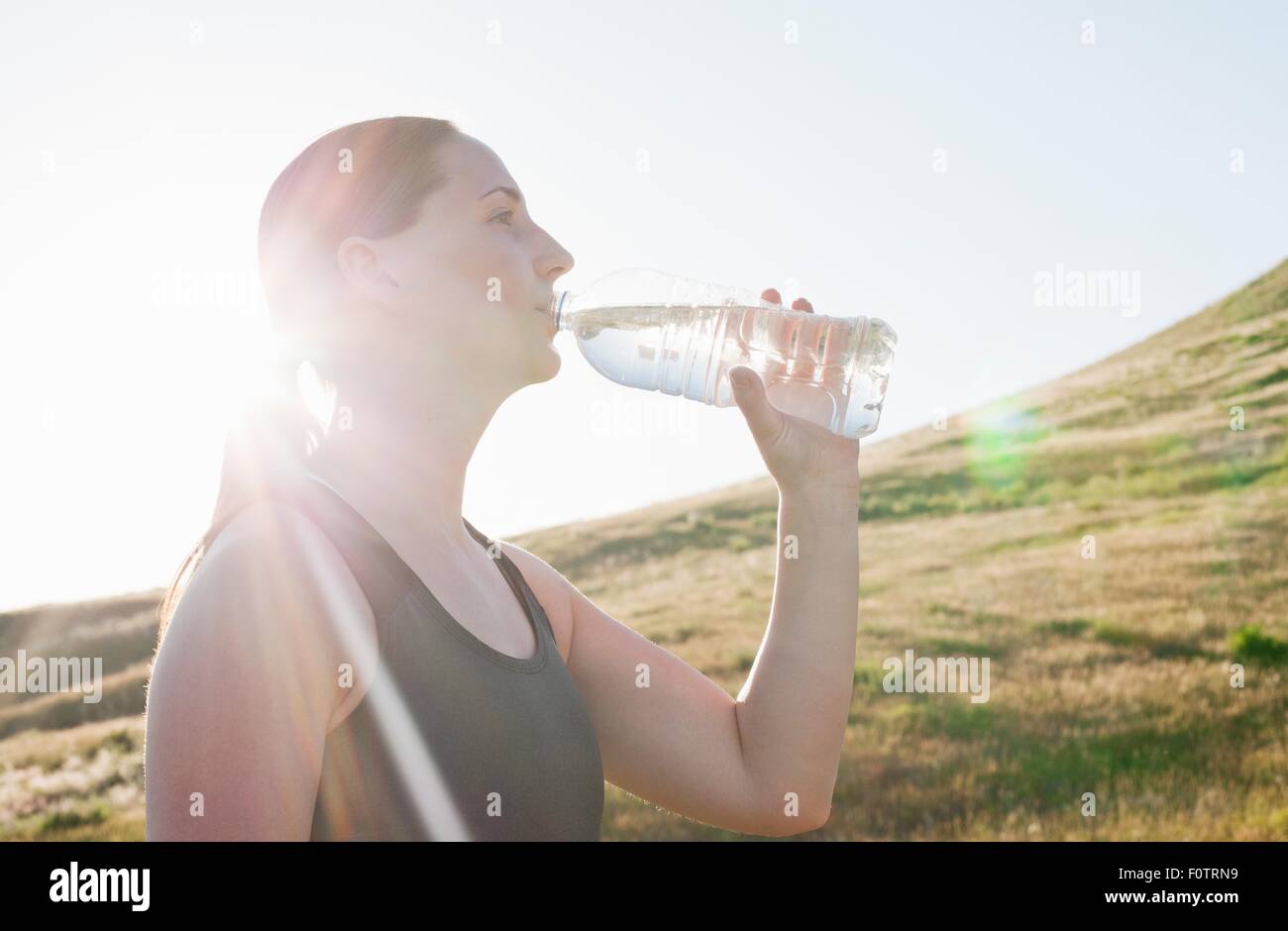 Young female runner drinking bottled water on sunlit hillside Stock Photo