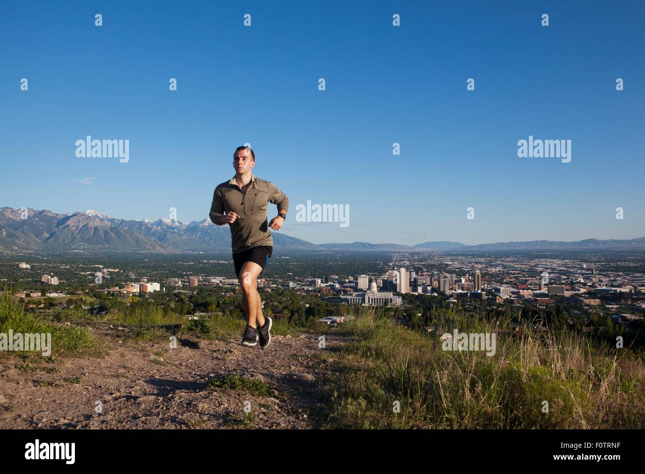Young male runner running along track above city in valley Stock Photo