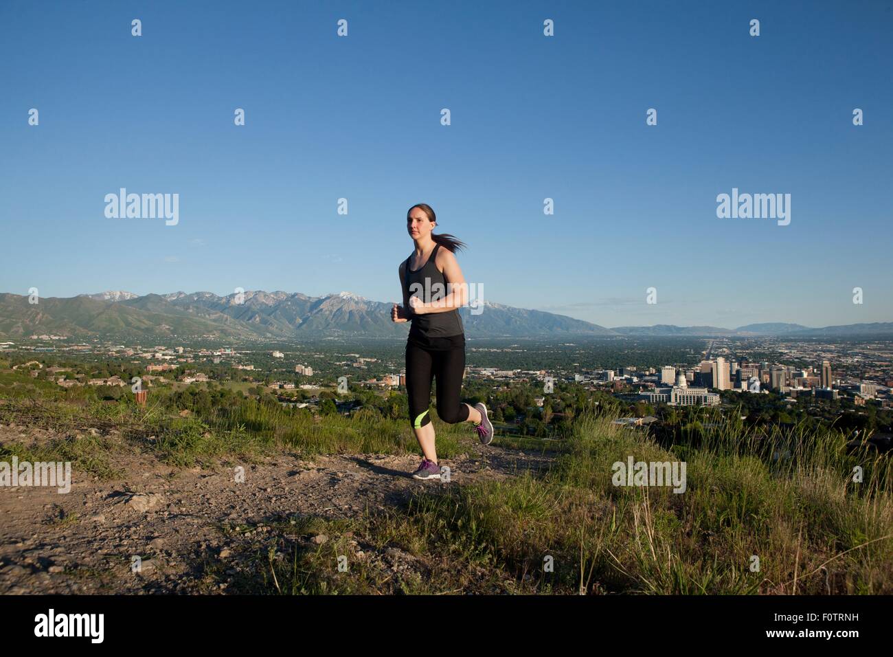 Young female runner running along track above city in valley Stock Photo