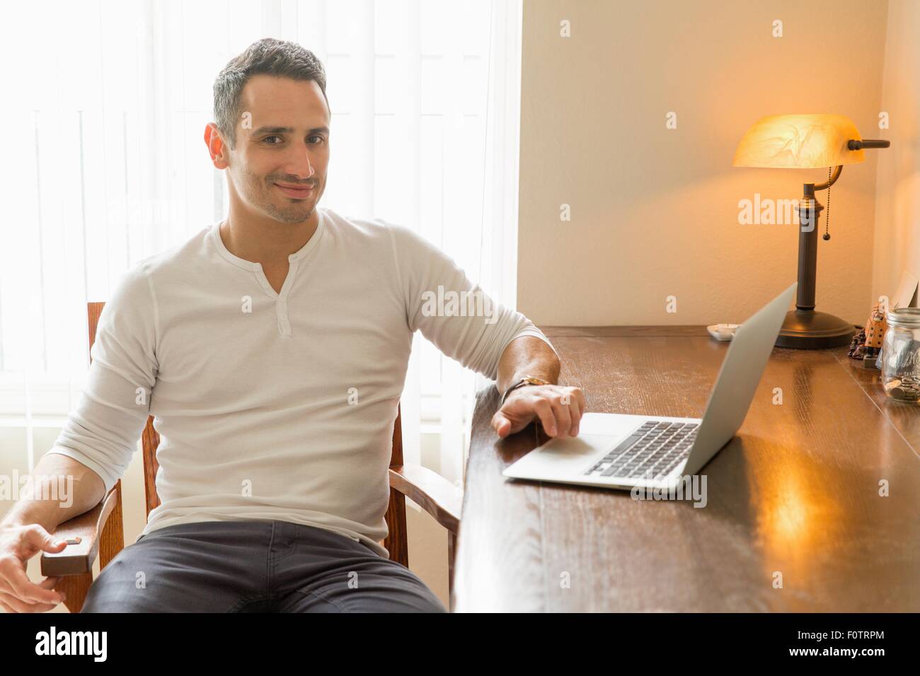 Mid adult man sitting at desk, using laptop Stock Photo